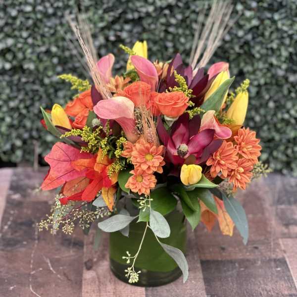 Colorful autumn bouquet in a green vase with orange, pink, yellow, and burgundy flowers