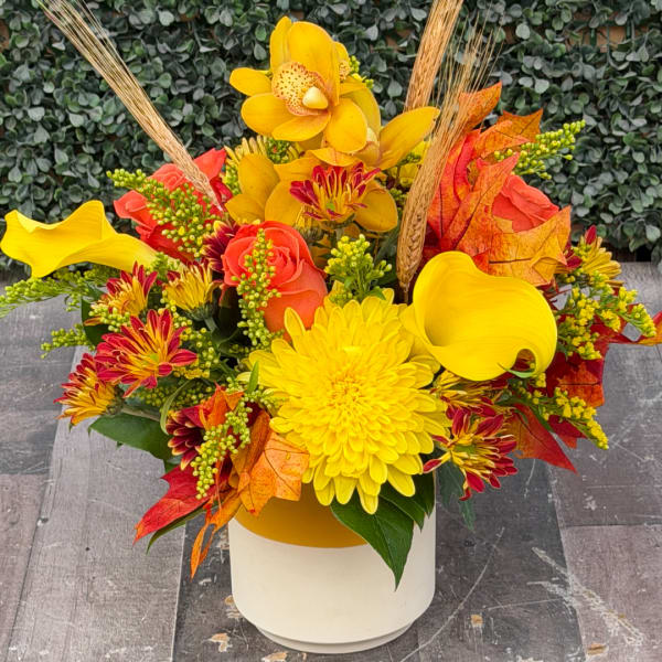 Yellow and orange floral arrangement in a white vase with autumn leaves