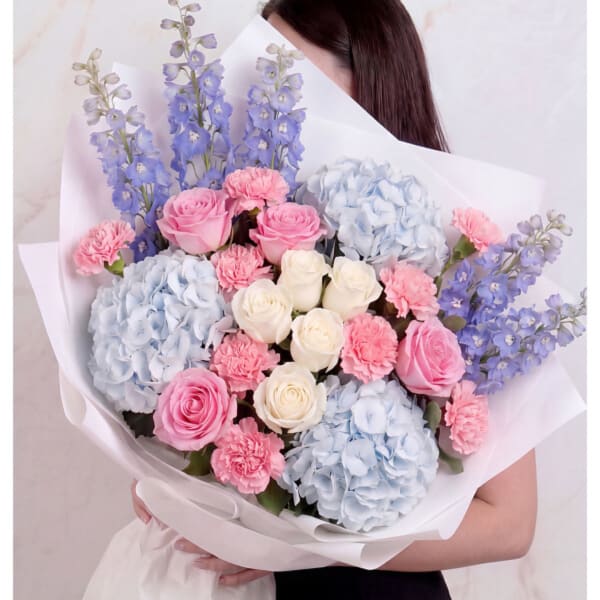 Bouquet of pink roses, blue hydrangeas, and purple delphinium in white wrap
