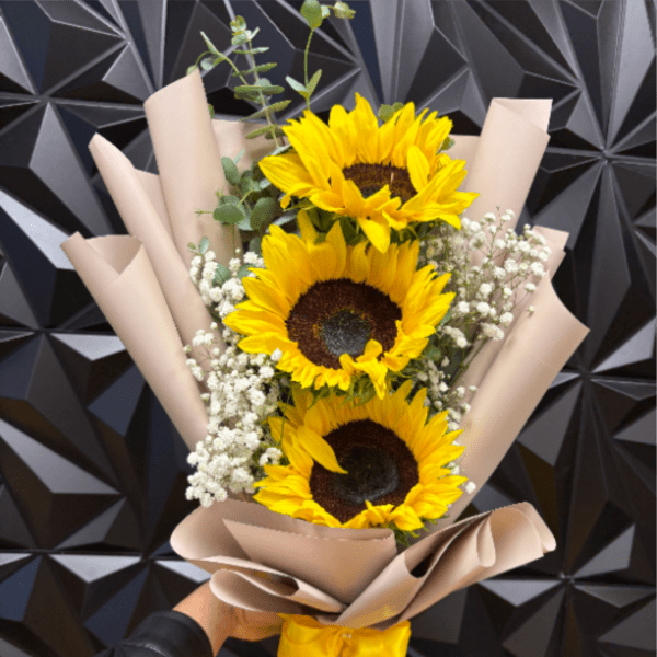 Wrapped bouquet of three yellow sunflowers with white filler flowers and a yellow ribbon.
