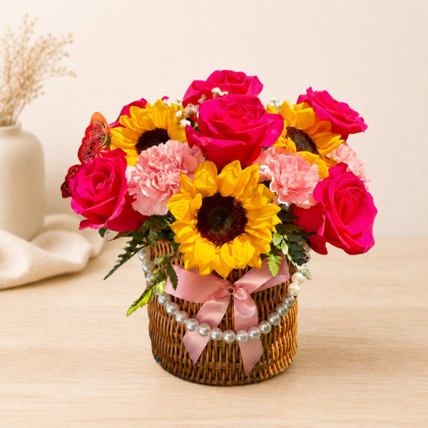 Pink roses and sunflowers in a wicker basket with a pink ribbon