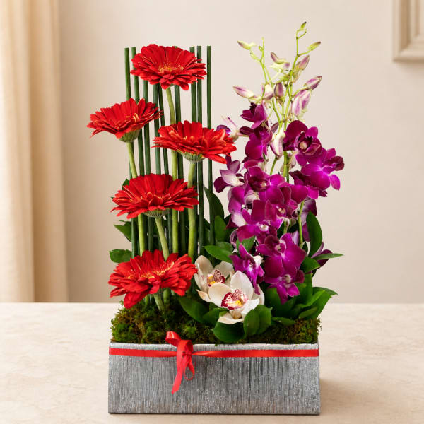 Red gerbera daisies and purple orchids in a silver rectangular planter