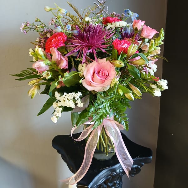 Mixed bouquet of pink, purple, and white flowers in a glass vase with a ribbon
