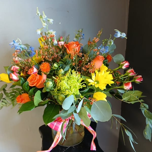 Mixed bouquet with orange roses, yellow daisies, and blue flowers in a glass vase