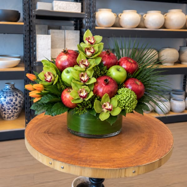 Fruit and orchid arrangement in a green glass vase