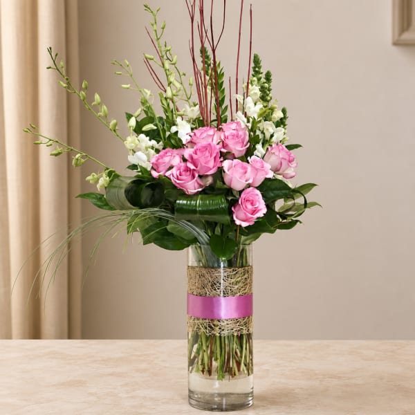 Pink roses and white snapdragons in a tall glass vase with a pink ribbon