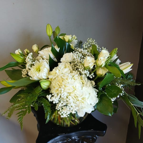 White floral arrangement in a glass vase with lilies, roses, and hydrangeas