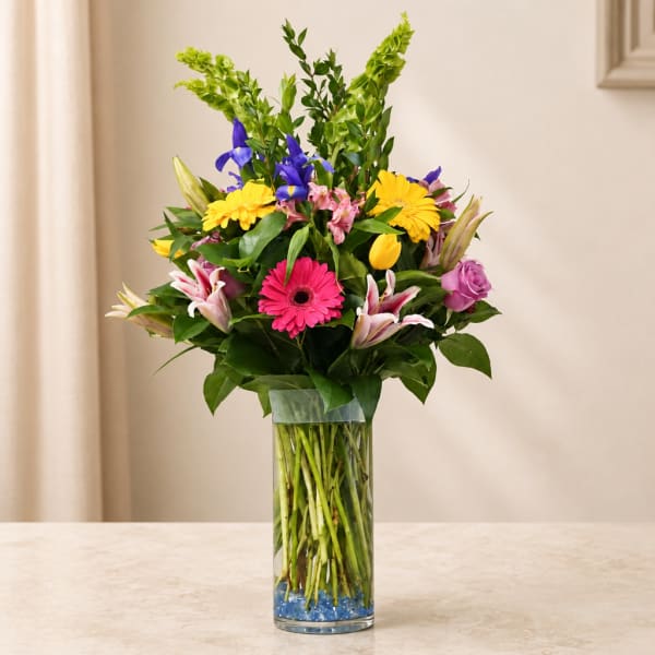 Mixed bouquet in a clear glass vase with pink, yellow, purple, and white flowers