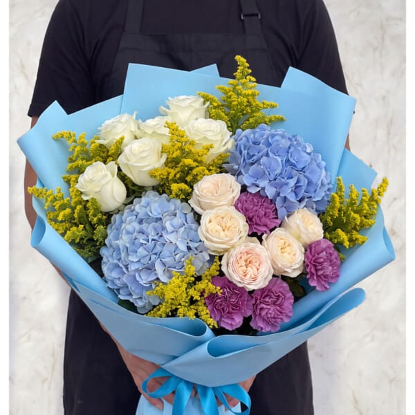 Bouquet of blue hydrangeas, white roses, and purple carnations wrapped in blue paper