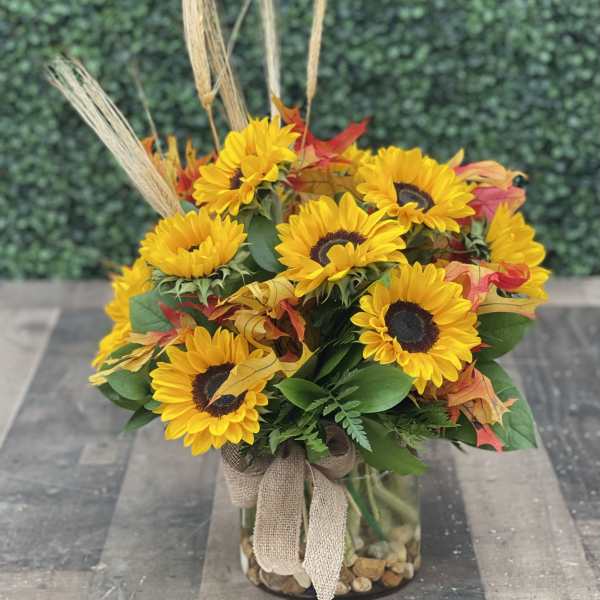 Sunflower arrangement in a glass vase with autumn leaves and burlap ribbon