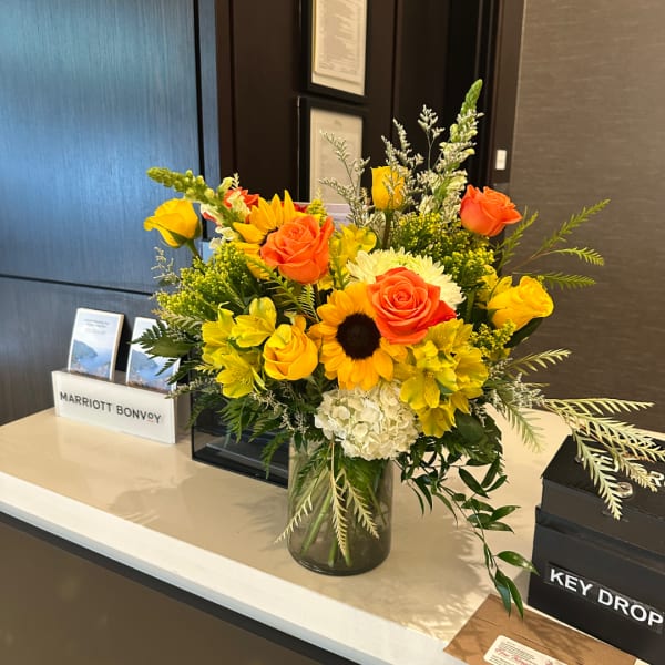 Mixed bouquet of yellow and orange roses with a sunflower in a glass vase