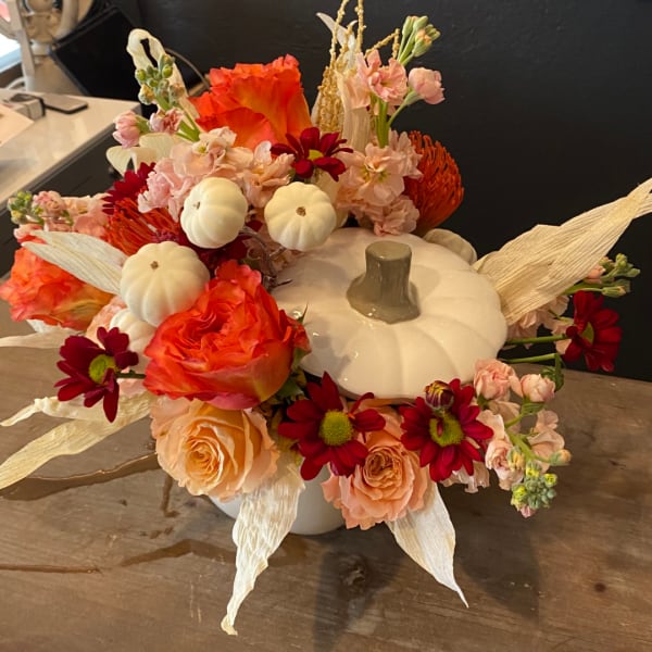 Pumpkin-shaped centerpiece with orange and peach flowers and white mini pumpkins