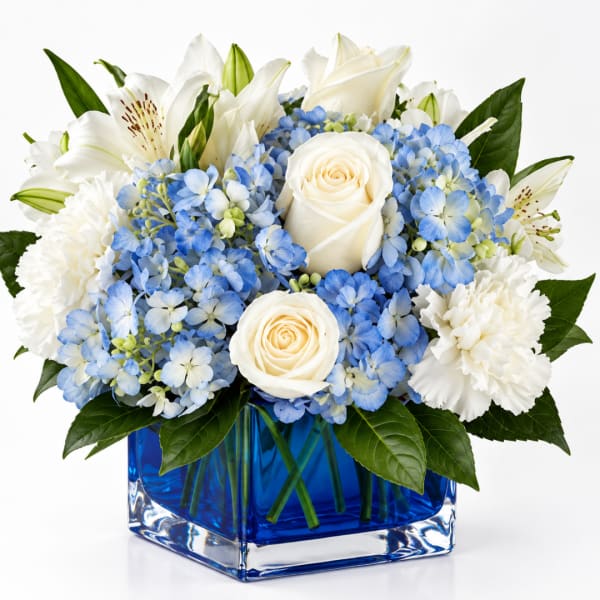 White roses and lilies with blue hydrangeas in a blue glass vase
