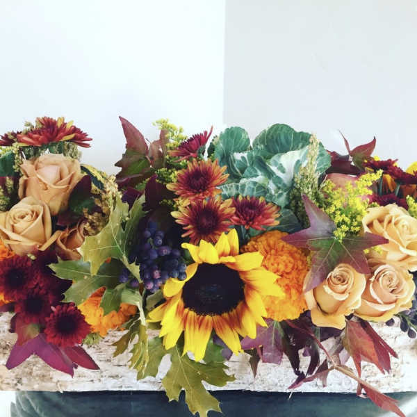 Autumn floral arrangement with sunflowers, roses, and chrysanthemums in a low container