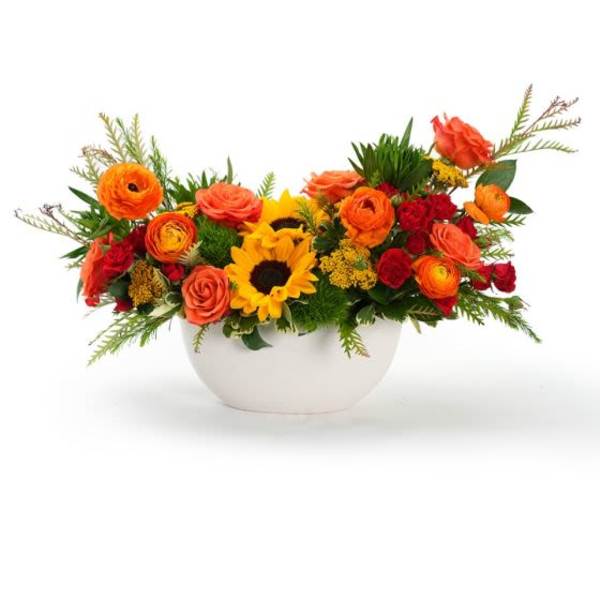 Low centerpiece with yellow sunflowers, orange roses, and red blooms in a white bowl.