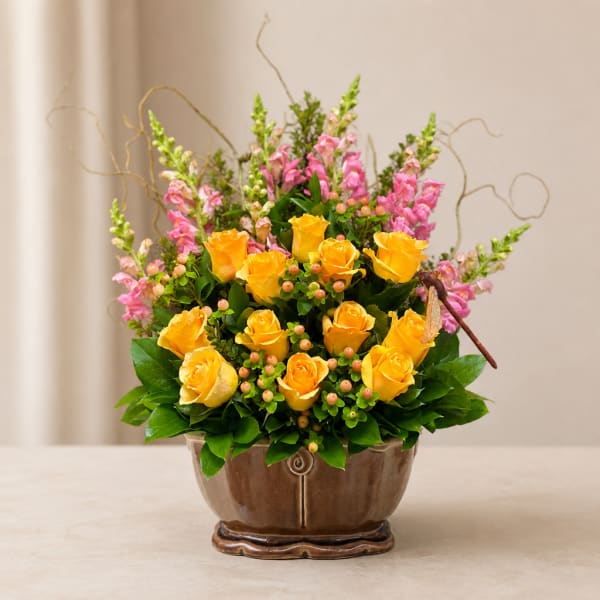 Yellow roses and pink snapdragons in a brown ceramic vase