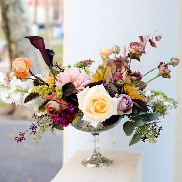Mixed floral arrangement in a silver goblet vase with roses and calla lilies