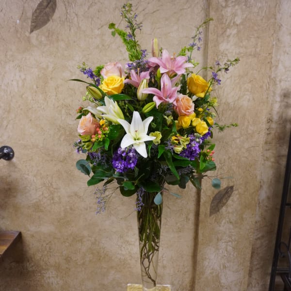 Mixed bouquet of lilies, roses, and purple flowers in a tall glass vase