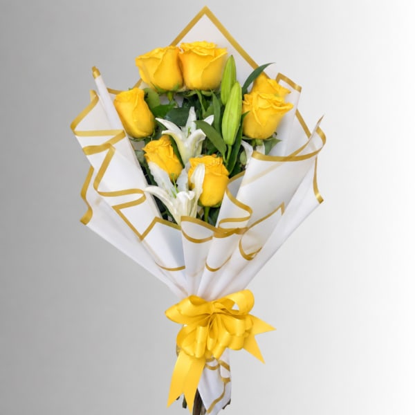 Bouquet of yellow roses and white lilies wrapped in white paper with gold trim