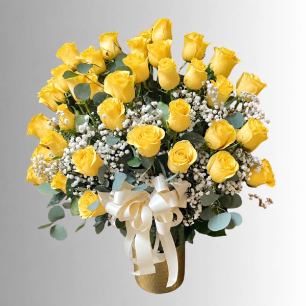Yellow roses arranged in a gold vase with white baby's breath and a ribbon bow