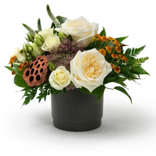 Low arrangement of ivory roses and small orange flowers in a black pot with a lotus pod accent