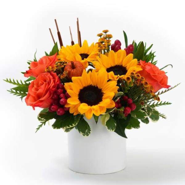 Low arrangement of yellow sunflowers and orange roses with red berries in a white vase