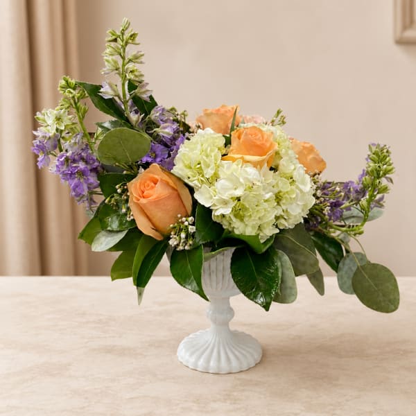 Peach roses and white hydrangeas in a white pedestal vase