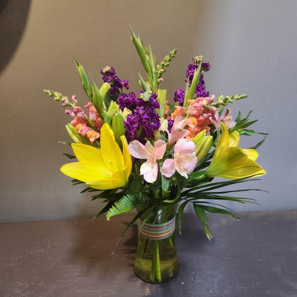 Mixed bouquet of yellow lilies, pink alstroemeria, and purple stock in a glass vase