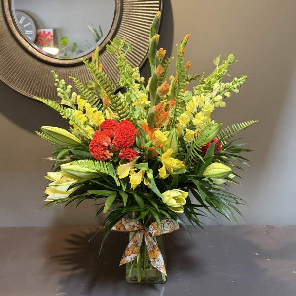 Mixed bouquet of yellow and red flowers in a glass vase with a decorative ribbon