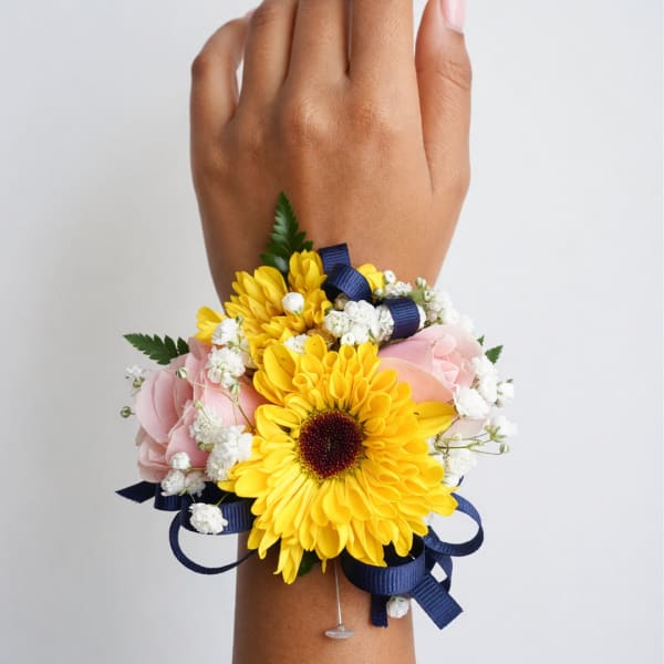 Yellow and pink floral wrist corsage with navy ribbon on a wrist