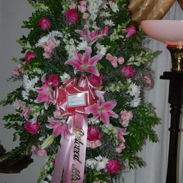 Tall standing floral spray with pink lilies and roses on a ribboned easel