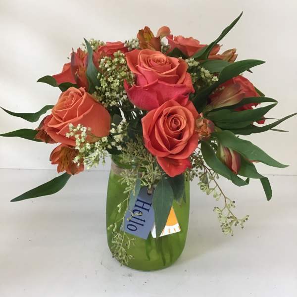 Coral and pink roses in a green glass vase with mixed greenery