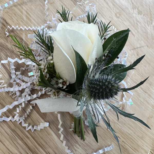 White rose boutonniere with greenery and ribbon on a wood surface