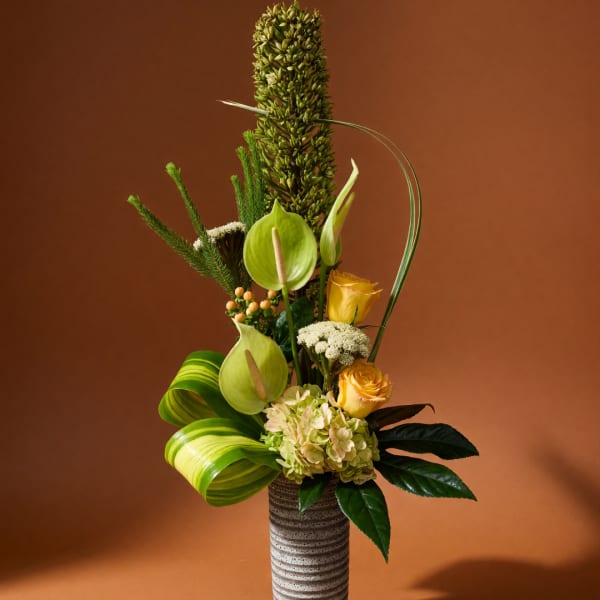Tall floral arrangement with yellow roses and green anthuriums in a striped vase