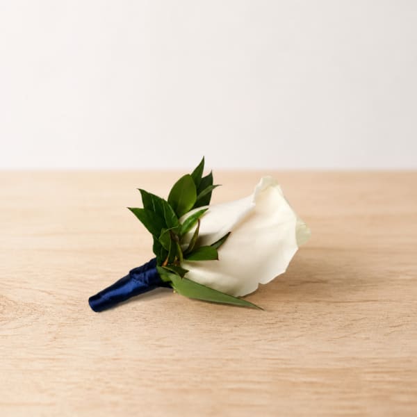 White rose boutonniere with green leaves and a navy ribbon wrap