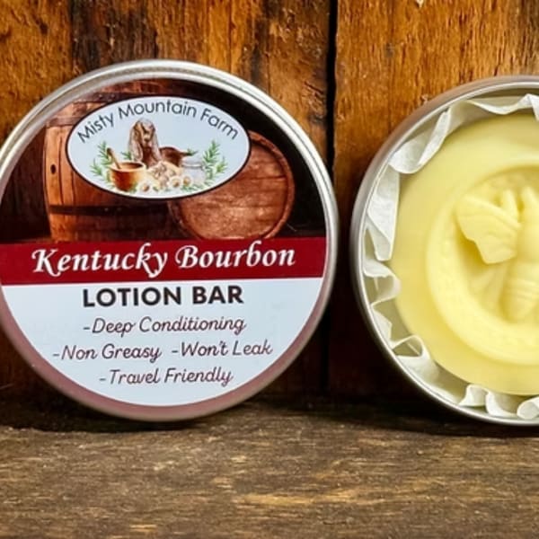 Two round tins of lotion bar on a wooden surface, one labeled Kentucky Bourbon.
