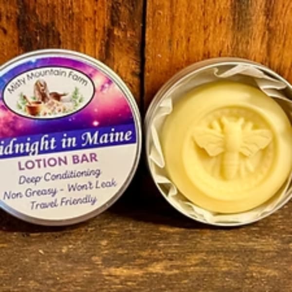 Two round lotion bars in tins on a wooden surface, one labeled and one with an embossed butterfly.