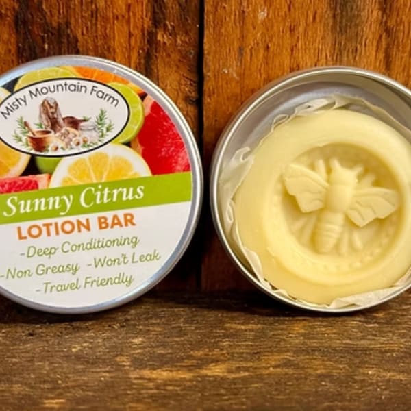 Tin of citrus lotion bar beside its labeled lid on a wooden surface.