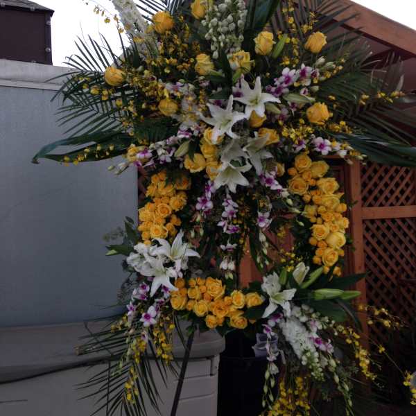 Large standing floral spray with yellow roses, white lilies, and orchids