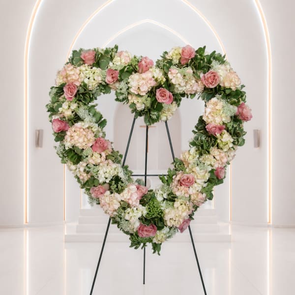 Heart-shaped floral wreath with pink roses and pale hydrangeas on a stand