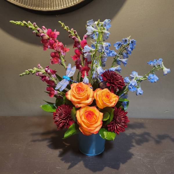 Orange roses with blue and pink flowers in a blue container