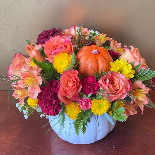 Mixed flower arrangement in a white pumpkin-shaped container with a small orange pumpkin centerpiece