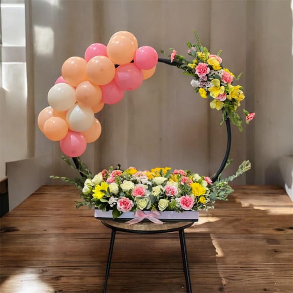 Floral arrangement with pink and peach balloons on a circular frame