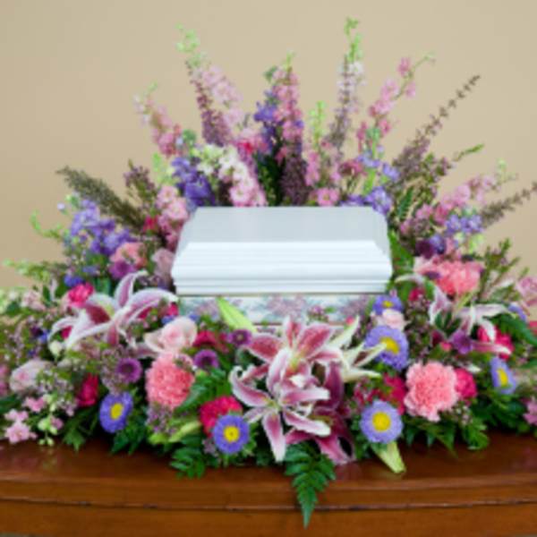 Casket spray with pink and purple flowers and white lilies