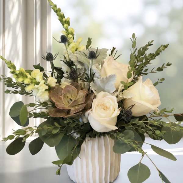 White roses and snapdragons in a ribbed vase with eucalyptus and succulents