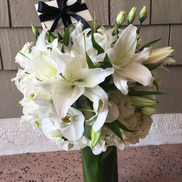White lilies and orchids in a tall glass vase with a black ribbon