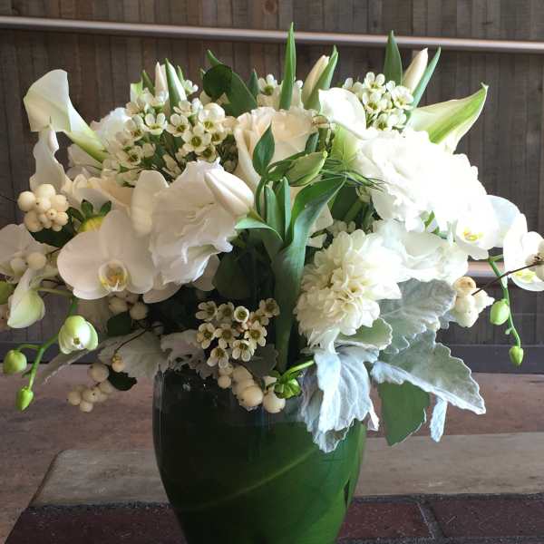 White floral arrangement in a glass vase with orchids and calla lilies