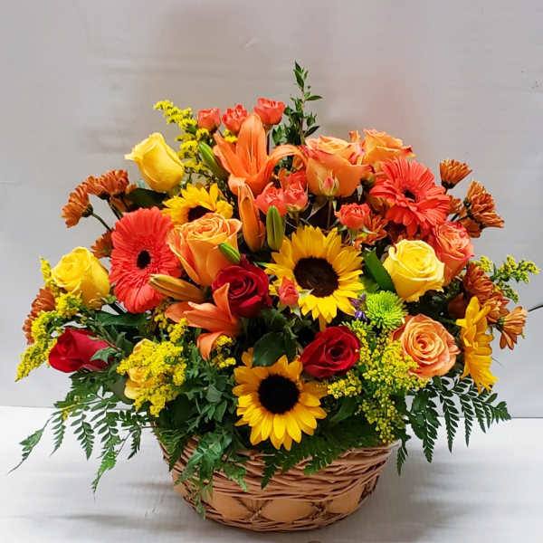Mixed bouquet of roses, lilies, sunflowers, and gerbera daisies in a wicker basket