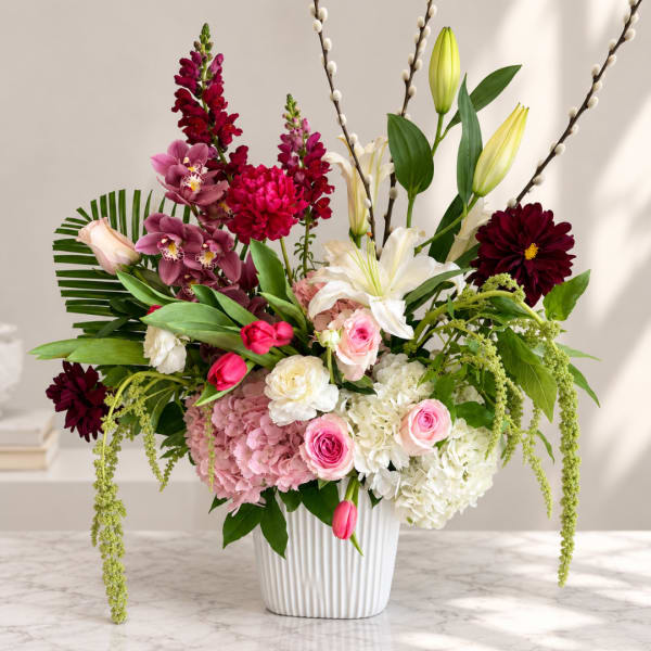 Mixed bouquet of lilies, roses, hydrangeas, and tulips in a white vase