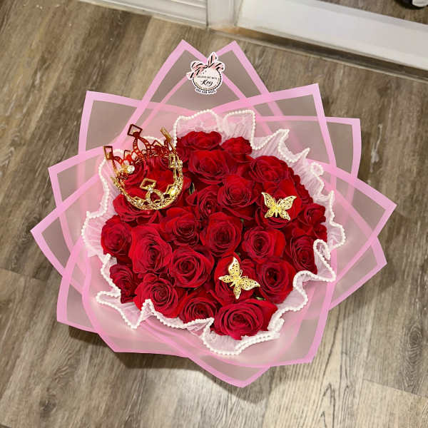Bouquet of red roses wrapped in pink paper with gold crown accents